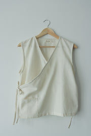 Natural off-white hemp cotton wrap top hanging on wooden hanger, minimalist design with front pocket and side ties, perfect for eco-conscious summer fashion.