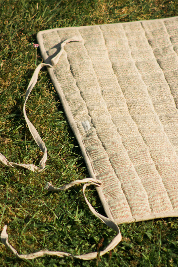 Yoga mat rolled out on grass, showing cotton tie straps for easy rolling.