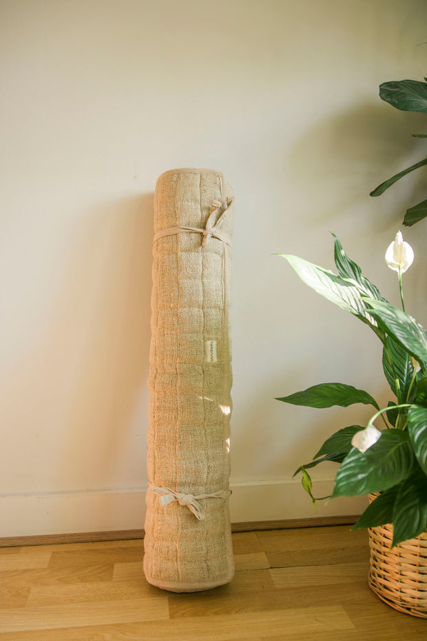 Rolled-up hemp yoga mat standing vertically beside indoor plants.